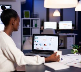 African businesswoman working with financial stats late at night in the office. Focused employee doing overtime for job respecting deadline of project writing, searching.