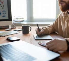 Close-up of busy brand designer sitting at desk and creating graphic design using digitizer and color palette